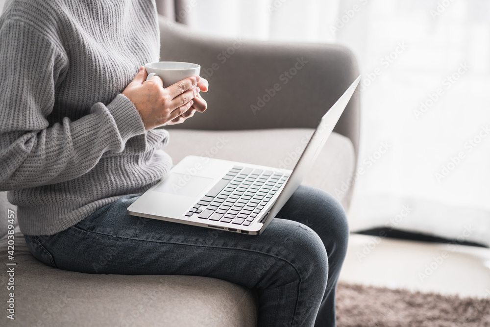 Naklejka premium women sitting relax on sofa holding coffee mug white with computer laptop at living room, new normal lifestyle, work from home concept.
