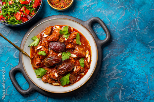 Traditional Moroccan lamb tagine simmered in spices, with dates and almonds. Salad and spices. Blue background. photo