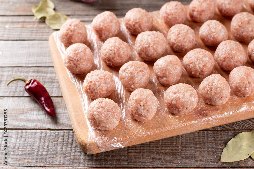 Side view closeup on raw semi-finished frozen meatballs on the wooden board with rice, onion and meat, horizontal Side view closeup on raw semi-finished frozen meatballs on the wooden board with rice, onion and meat, horizontal