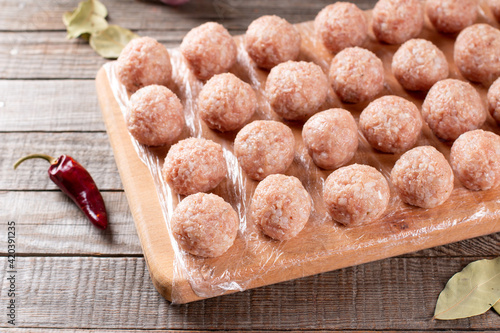 Side view closeup on raw semi-finished frozen meatballs on the wooden board with rice, onion and meat, horizontal photo