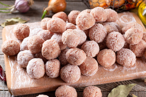 Side view closeup on raw semi-finished frozen meatballs on the wooden board with rice, onion and meat, horizontal photo