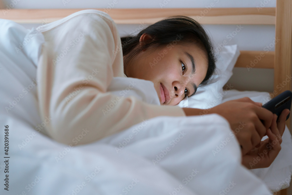 Asian woman using a smartphone while lying in the bedroom at the night. Asian woman using a smartphone while lying in the bedroom at the night.