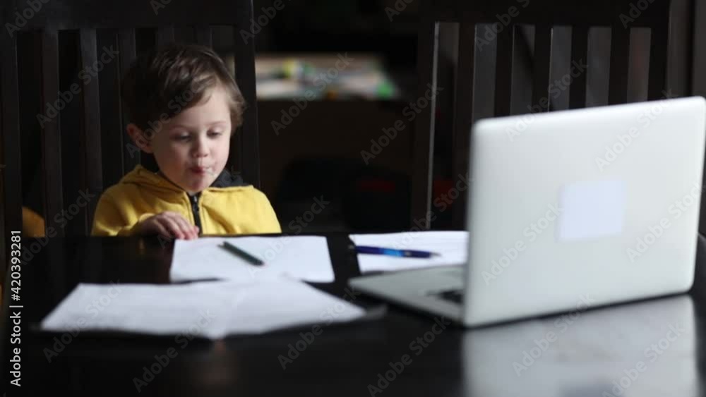 Little boy siting at table with laptop and documents for lesson at home