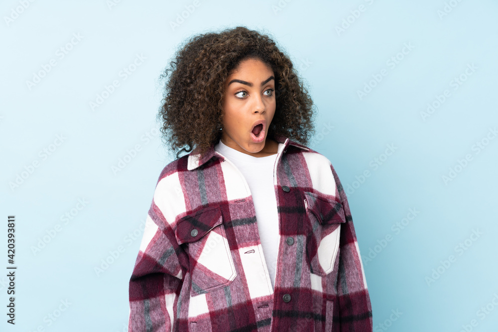 Young African American woman isolated on blue background doing surprise gesture while looking to the side Young African American woman isolated on blue background doing surprise gesture while looking to the side