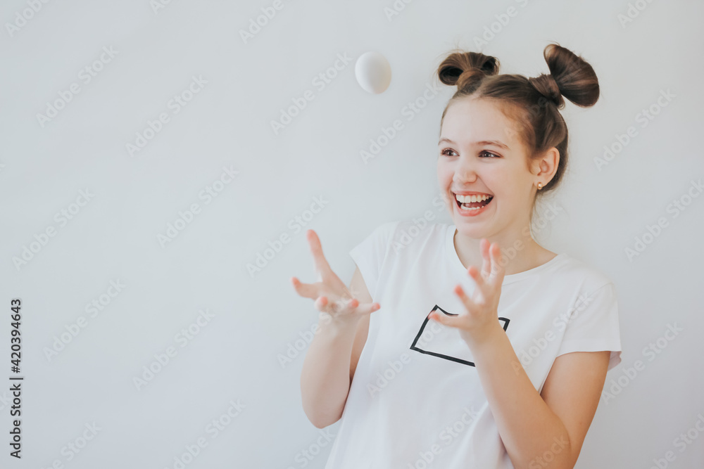 A cute happy teenage girl with bunny ears made of her hair holding white eggs in her hands. Kid ready for Easter hunt party, going to paint eggs. Happy Easter, holiday, childhood concept.