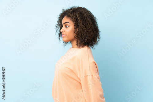 Young African American woman isolated on blue background in back position and looking back