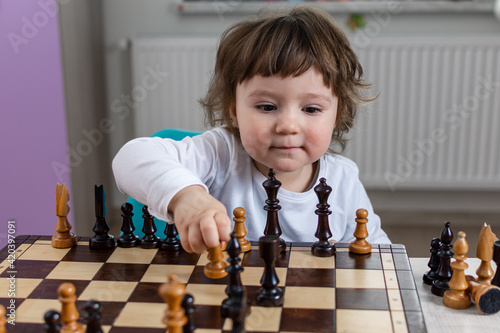 Mała dziewczynka z szachownicą. Dziecko uczy się grać w szachy.