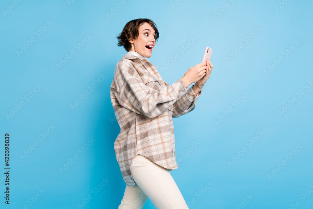 Profile side photo of young excited girl happy smile use cellphone like comment post isolated over blue color background Profile side photo of young excited girl happy smile use cellphone like comment post isolated over blue color background