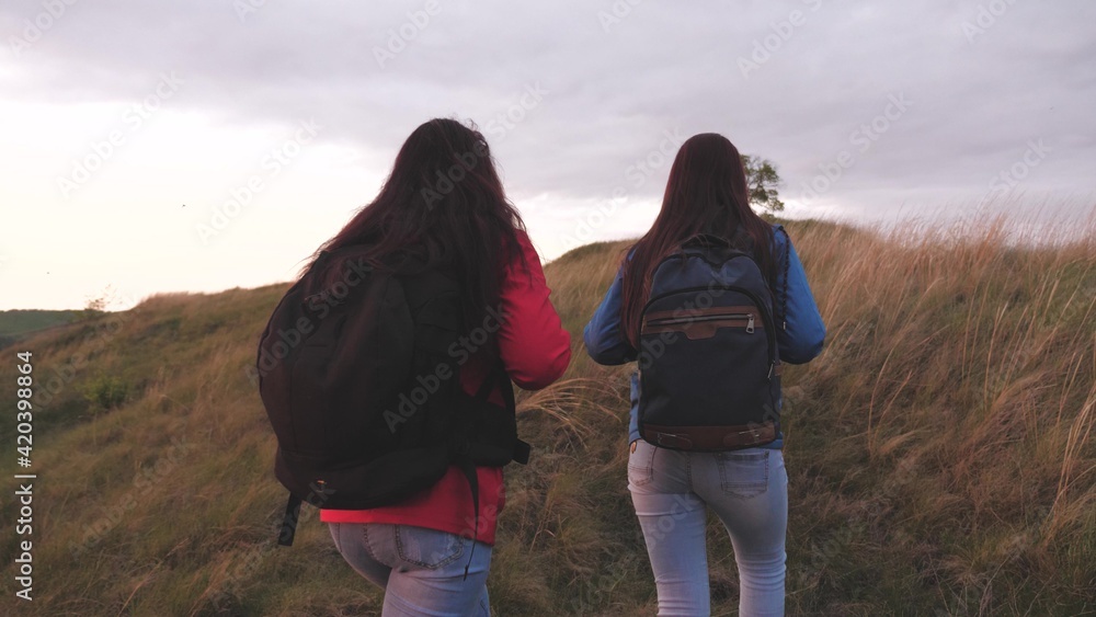 Girls with backpacks climb high up the mountain helping each other on a hiking trip. Women spend the weekend traveling in nature overcoming obstacles. Teamwork. Friends are looking for adventure