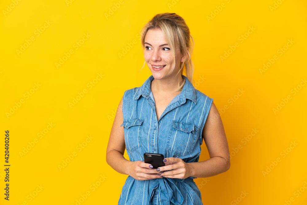 Young Russian woman isolated on yellow background using mobile phone and looking up Young Russian woman isolated on yellow background using mobile phone and looking up
