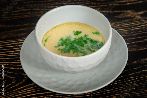 Creamy soup decorated with herbs in a gray bowl on a plate on a dark wooden table.