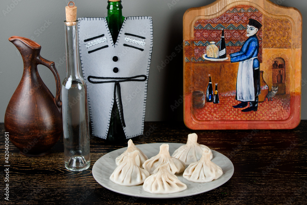 Khinkali on a gray plate against the background of bottles in a Georgian-style decoration, a jug, a board with a thematic pattern on a dark wooden table.