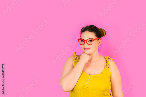 Mujer joven y alegre con el puño de la mano apoyado en el mentón sobre un fondo rosa fuerte liso y aislado. Vista de frente. Copy space