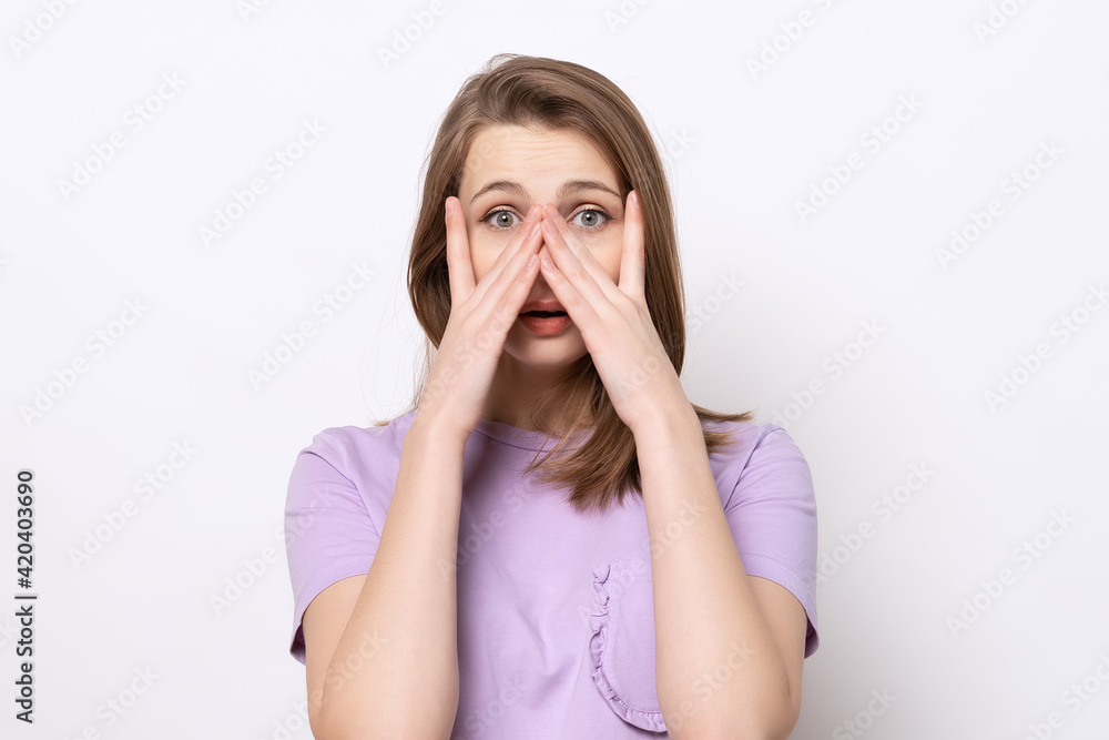 close up scared girl hiding face in palms hands and peering out with one eye between her fingers, trembling fear close up scared girl hiding face in palms hands and peering out with one eye between her fingers, trembling fear