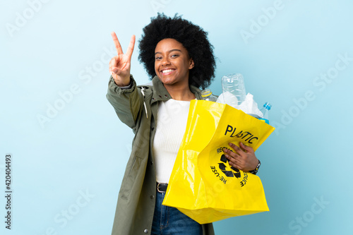 Young African American woman holding a recycle bag isolated on colorful background smiling and showing victory sign