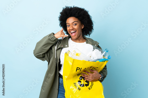 Young African American woman holding a recycle bag isolated on colorful background making phone gesture. Call me back sign