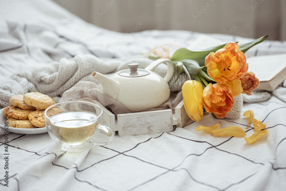 Spring home composition in bed with a cup of tea, cookies, a teapot, a book and a bouquet of flowers. Spring home composition in bed with a cup of tea, cookies, a teapot, a book and a bouquet of flowers.