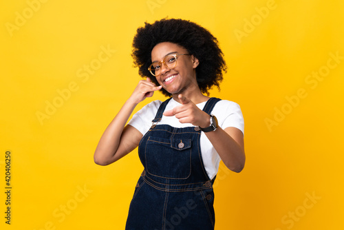 Young African American woman isolated on yellow background making phone gesture and pointing front