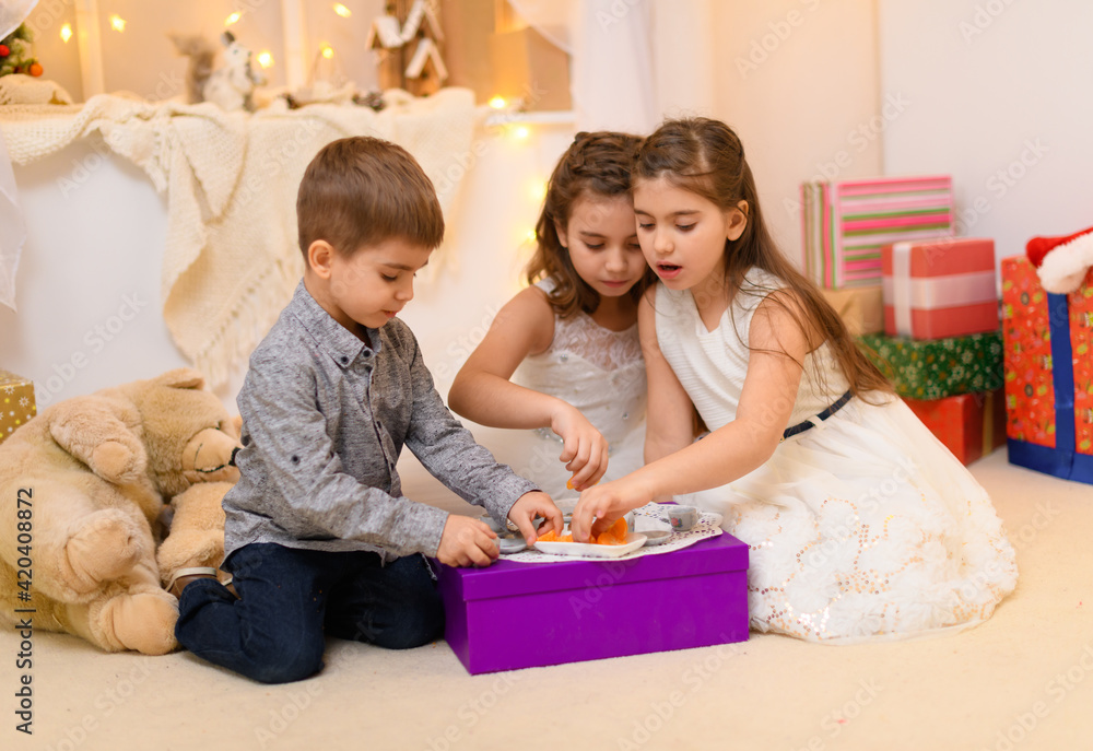 children drink tea, eat cookies and play with the toy dishes in home interior decorated with holiday lights and gifts children drink tea, eat cookies and play with the toy dishes in home interior decorated with holiday lights and gifts