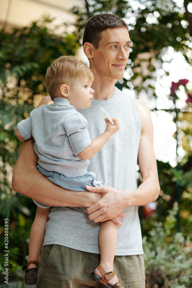 Young father holding his little son in his arms while standing in the city outdoors Young father holding his little son in his arms while standing in the city outdoors