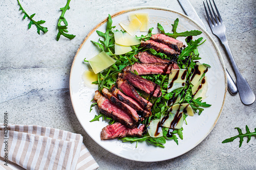 Photos Beef steak tagliata with arugula and parmesan on gray plate, gray background, top view