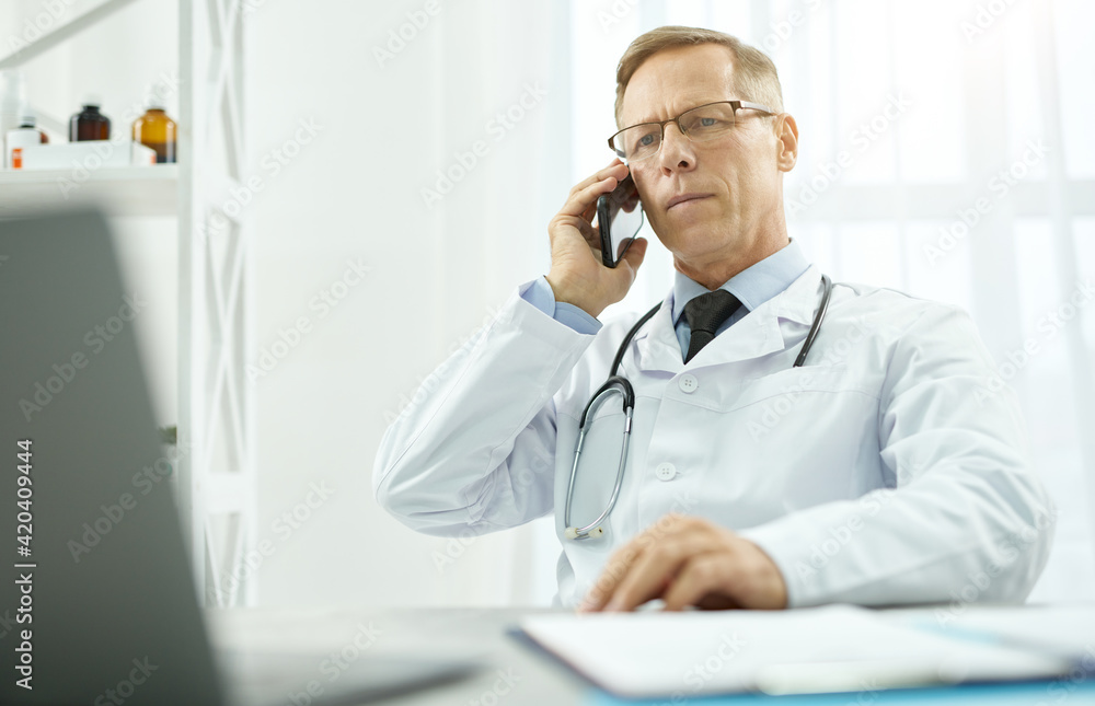 Handsome male doctor having phone conversation in clinic