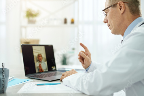 Male doctor giving online consultation to old woman in clinic
