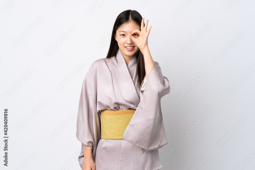 Young Chinese girl wearing kimono over isolated background showing ok sign with fingers Young Chinese girl wearing kimono over isolated background showing ok sign with fingers