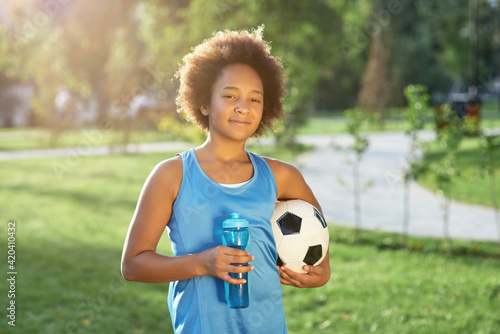 Cute girl with soccer ball and bottle of water standing on the street