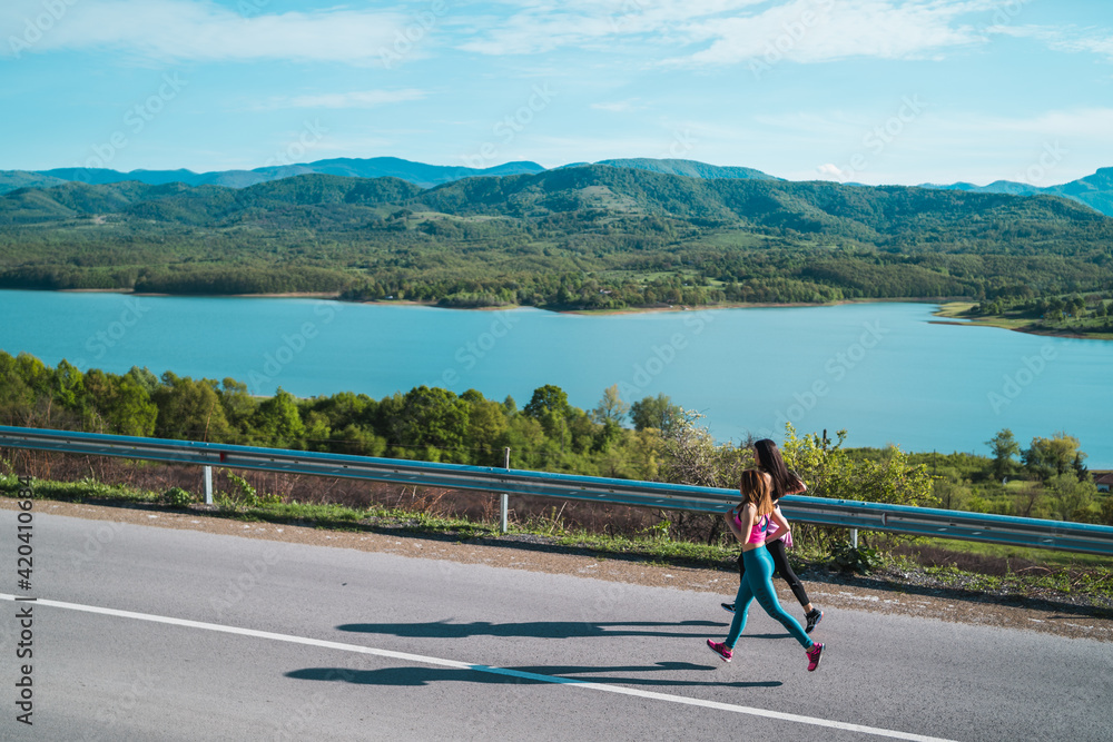 Fit female athletes running jogging on asphalt road near lake
