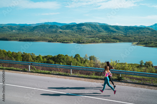 Fit female athletes running jogging on asphalt road near lake