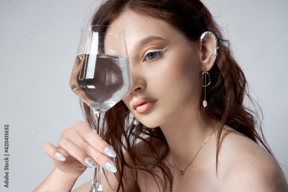 Young adult woman holds a glass of water in her hand near face. Beautiful makeup, clean skin Young adult woman holds a glass of water in her hand near face. Beautiful makeup, clean skin