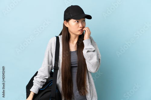 Young sport Chinese woman with sport bag over isolated blue background is a little bit nervous
