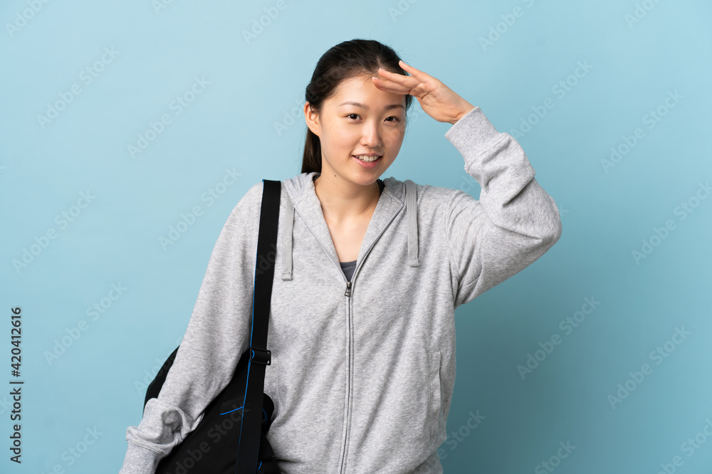 Young sport Chinese woman with sport bag over isolated blue background looking far away with hand to look something Young sport Chinese woman with sport bag over isolated blue background looking far away with hand to look something