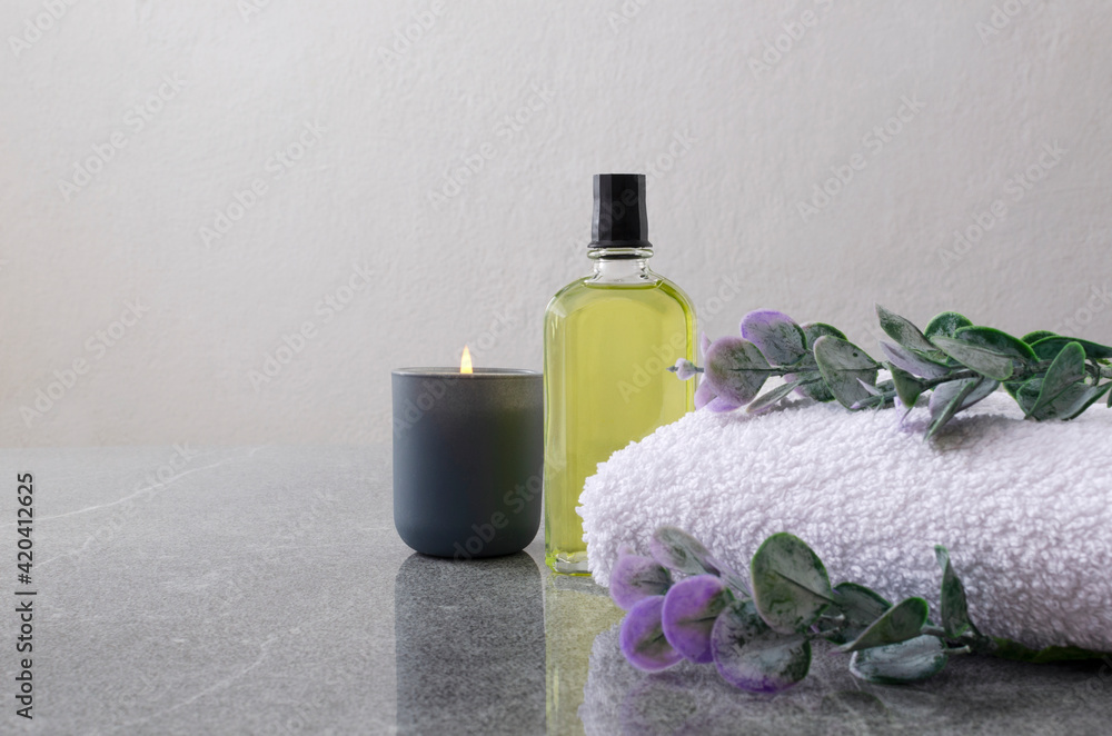 Relaxation concept.White towel, massage oil, candle and eucalyptus leaves on the grey surface.Empty space Relaxation concept.White towel, massage oil, candle and eucalyptus leaves on the grey surface.Empty space