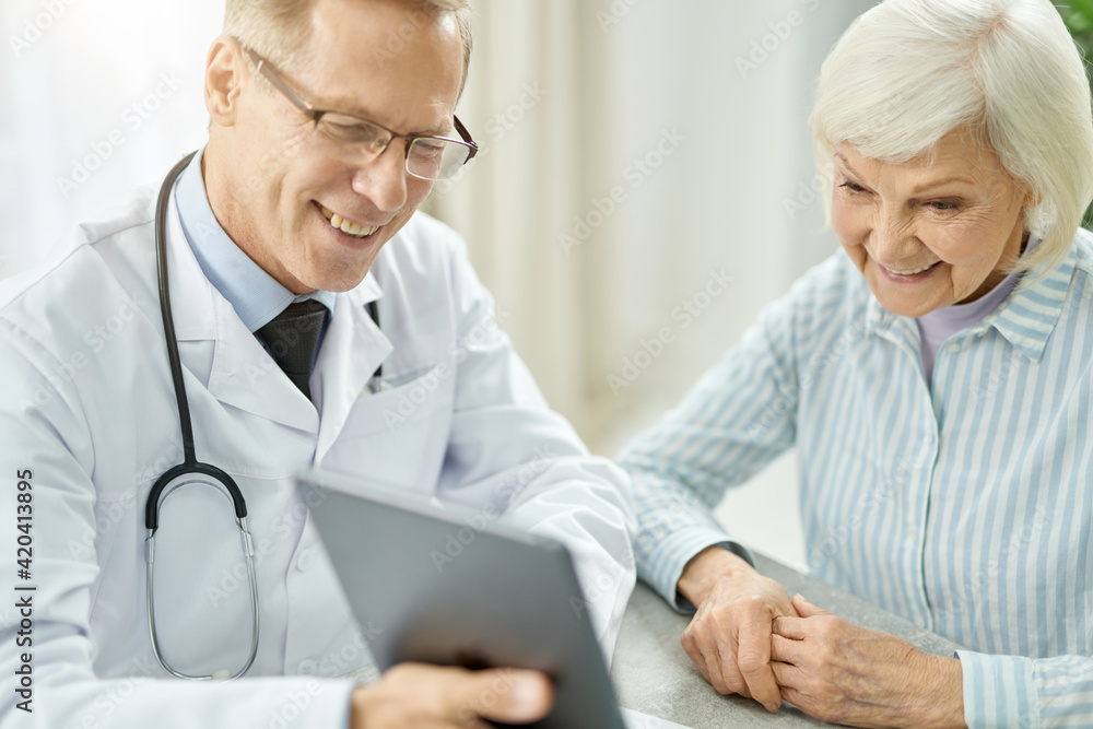 Cheerful doctor using tablet computer while talking with old lady Cheerful doctor using tablet computer while talking with old lady