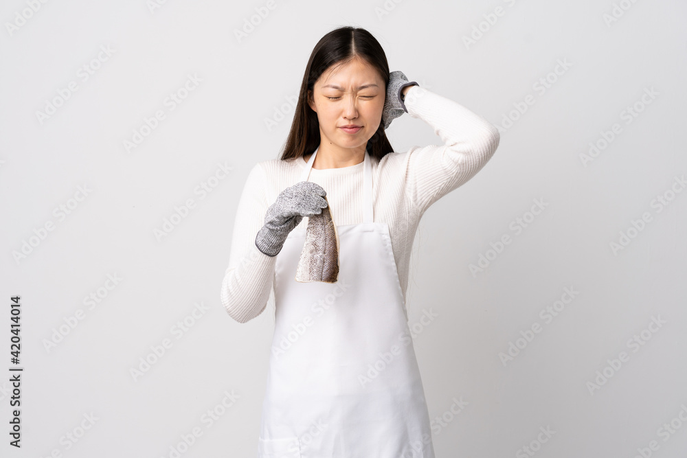 Chinese fishmonger wearing an apron and holding a raw fish over isolated white background frustrated and covering ears Chinese fishmonger wearing an apron and holding a raw fish over isolated white background frustrated and covering ears