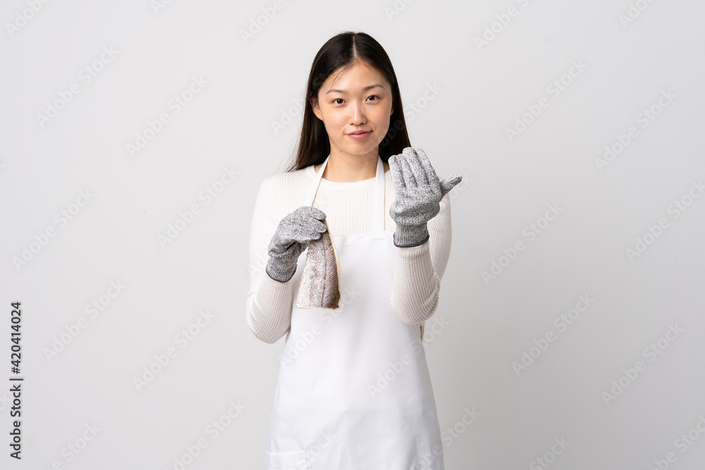 Chinese fishmonger wearing an apron and holding a raw fish over isolated white background inviting to come with hand. Happy that you came Chinese fishmonger wearing an apron and holding a raw fish over isolated white background inviting to come with hand. Happy that you came
