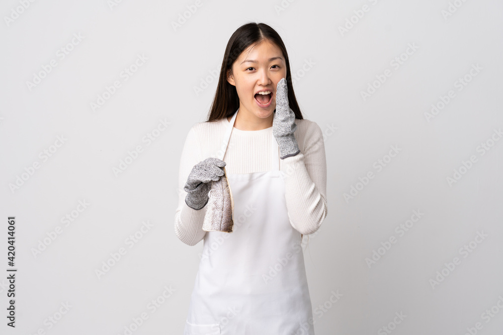 Chinese fishmonger wearing an apron and holding a raw fish over isolated white background shouting with mouth wide open Chinese fishmonger wearing an apron and holding a raw fish over isolated white background shouting with mouth wide open