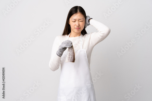 Chinese fishmonger wearing an apron and holding a raw fish over isolated white background frustrated and covering ears
