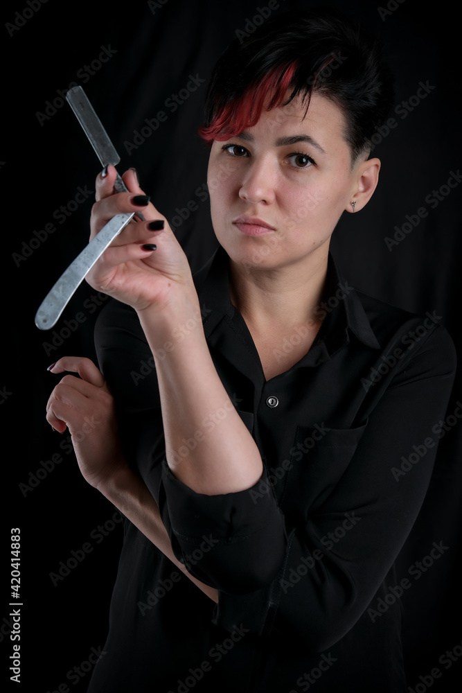 Obraz premium Half-length portrait of young adult barber woman on black background holding vintage straight razor, modern barber girl concept