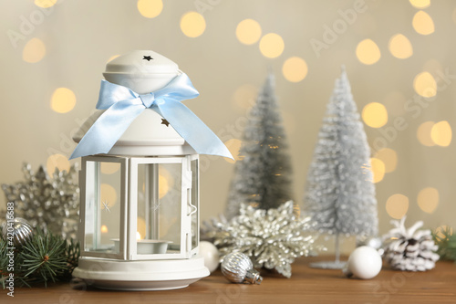 Christmas lantern with burning candle and festive ornaments on wooden table against blurred lights. Space for text © New Africa