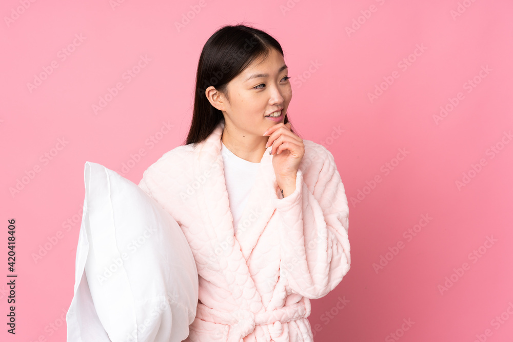 Young Asian woman in pajamas isolated on pink background thinking an idea and looking side Young Asian woman in pajamas isolated on pink background thinking an idea and looking side