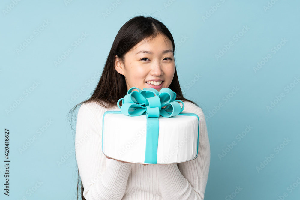 Pastry asian chef holding a big cake isolated on blue background Pastry asian chef holding a big cake isolated on blue background