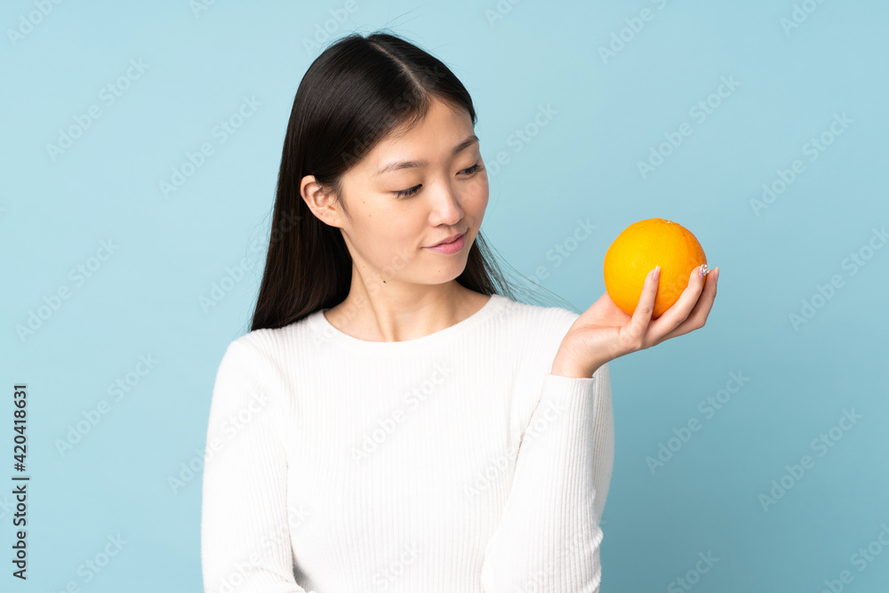 Young asian woman holding an orange over isolated blue background Young asian woman holding an orange over isolated blue background