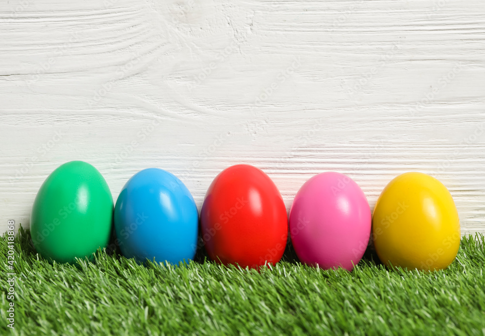 Bright Easter eggs on green grass against white wooden background Bright Easter eggs on green grass against white wooden background