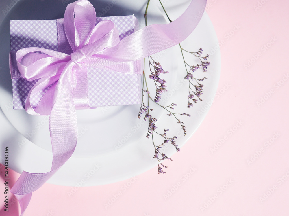 A gift box with a lilac ribbon lies on the plates saucers
