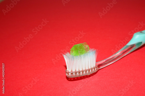 on a plastic transparent toothbrush lies light green toothpaste on a red background side view