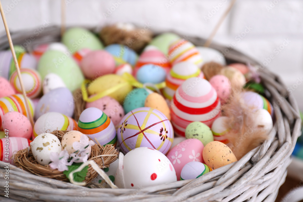 Fototapeta premium Many different Easter eggs in wicker basket on light background, closeup