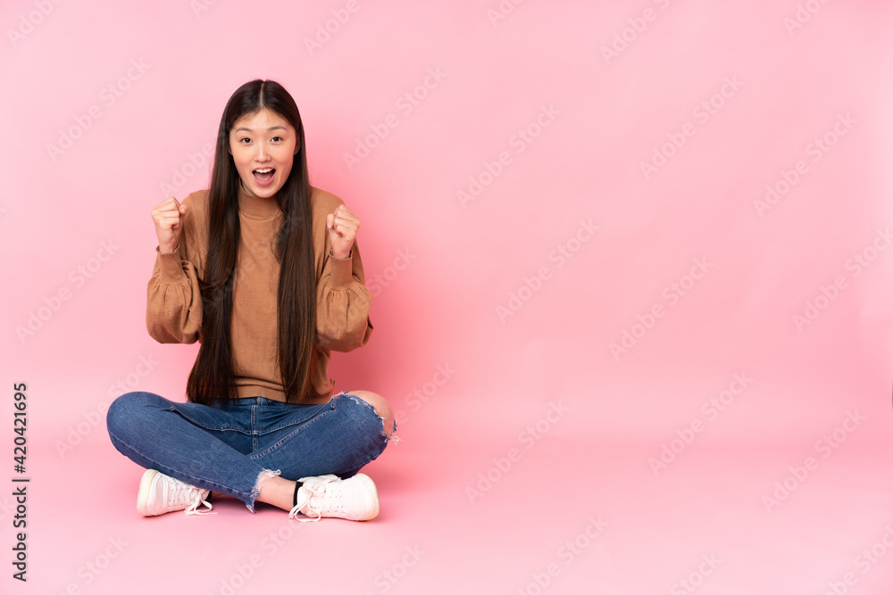 Young asian woman sitting on the floor isolated on pink background celebrating a victory in winner position Young asian woman sitting on the floor isolated on pink background celebrating a victory in winner position